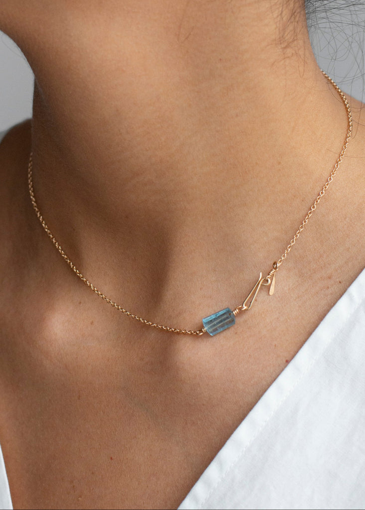 Necklace with a blue gemstone worn by a person against a neutral background